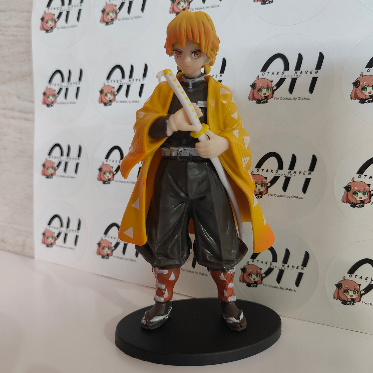 Anime character figurine with a yellow cloak and sword on a white background with brand logos.